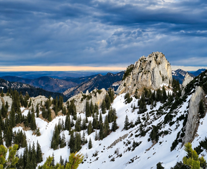 Schroffe Berglandschaft mit Schnee und Fichten unter bewölktem Himmel